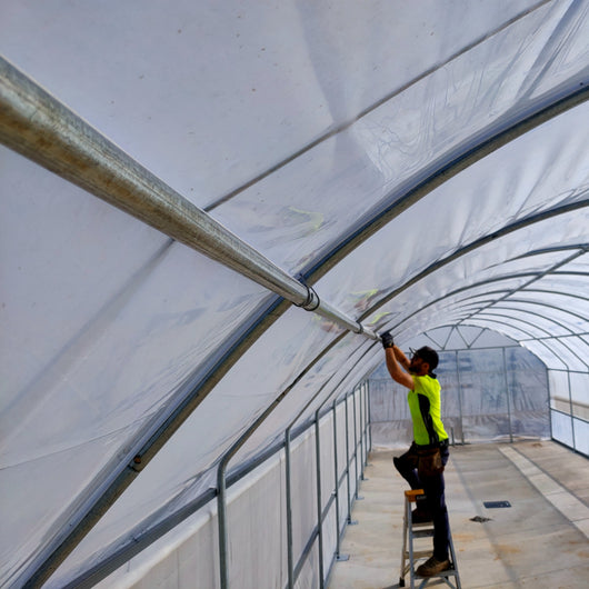 Person working on a large white tent structure inside a greenhouse.