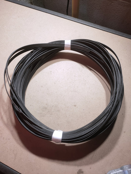 Coiled black tension rope wire on a cardboard surface